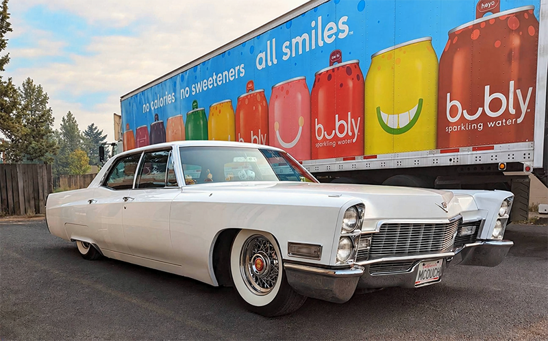 White Cadillac parked beside a colorful truck with the words all smiles