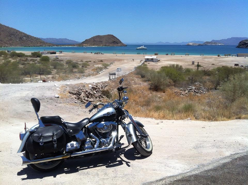 Motorcycle parked overlooking a beach and blue water on a Portland to Cabo trip